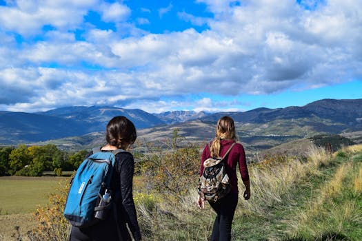 Two women hiking on a mountain trail with scenic views under a blue sky.